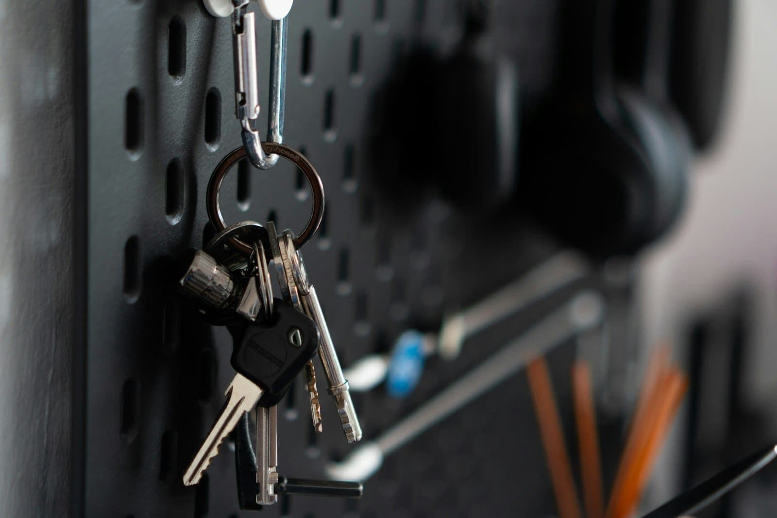 Bunch of keys on a carabiner hanging from a dark pegboard